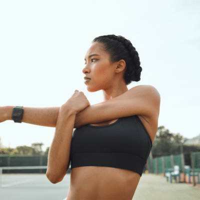 Motivated woman in athletic gear stretching while in deep thought.